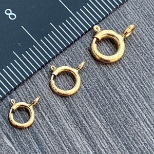 Pode incluir: Tr&ecirc;s an&eacute;is de salto de metal dourado de diferentes tamanhos. Os an&eacute;is est&atilde;o sobre uma superf&iacute;cie de madeira com uma r&eacute;gua no fundo.