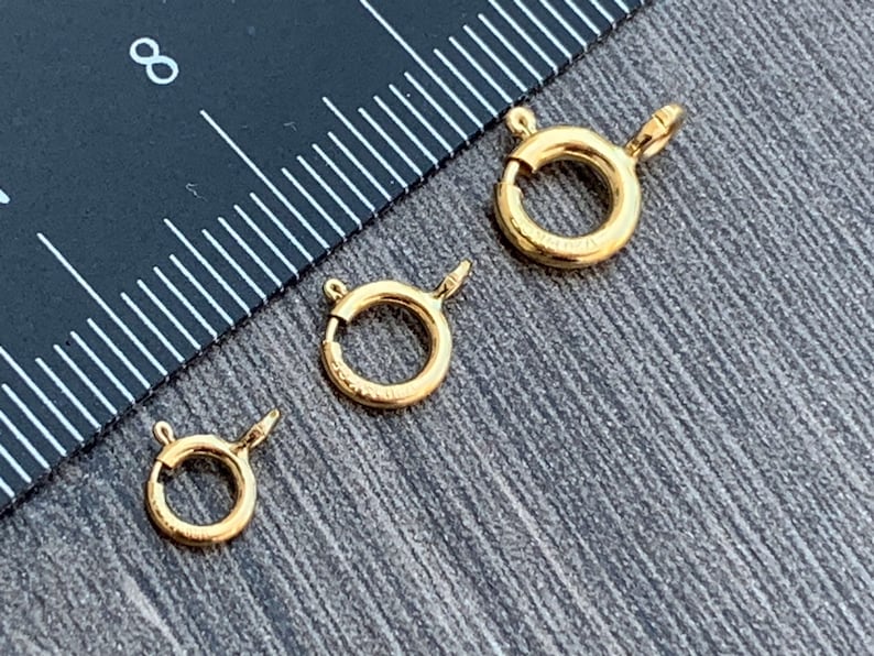 Pode incluir: Tr&ecirc;s an&eacute;is de salto de metal dourado de diferentes tamanhos. Os an&eacute;is est&atilde;o sobre uma superf&iacute;cie de madeira com uma r&eacute;gua no fundo.