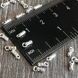 May include: A close-up of a ruler measuring 1 inch with silver metal jump rings scattered around it. The jump rings are about 1/4 inch in diameter.