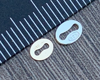 May include: Two oval-shaped metal charms, one gold and one silver. The gold charm has the inscription "1/20 14K" and the silver charm has the inscription "925".
