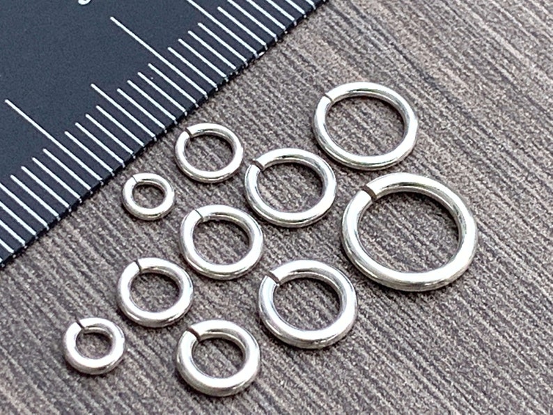 May include: Assortment of silver jump rings in various sizes. The jump rings are arranged on a wooden surface.