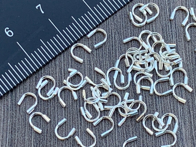 Op de afbeelding: Een close-up van een stapel zilverkleurige springringen. De ringen zijn klein en hebben een afgeronde vorm. Ze zijn perfect voor het maken van sieraden of andere knutselprojecten.