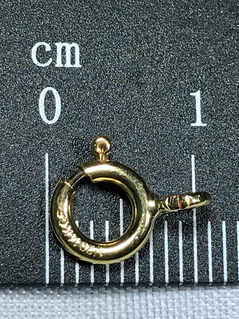 Pode incluir: Um anel de salto de metal dourado com um fecho de mola. O anel mede aproximadamente 1 cm de di&acirc;metro.