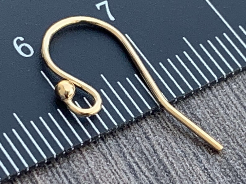 May include: Gold-toned earring hook with a small ball at the top. The hook is measured against a ruler.
