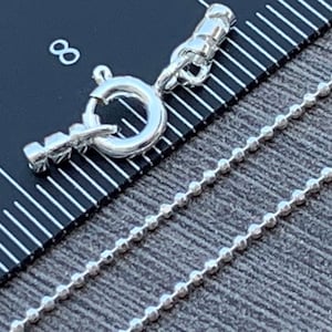 May include: A silver chain necklace with a lobster clasp closure. The chain is made of small, round beads.