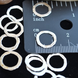 May include: A close-up of a group of silver metal rings, some stacked on top of each other. The rings are hammered and have a textured surface. A ruler is in the background, showing that the rings are about 1 inch in diameter.