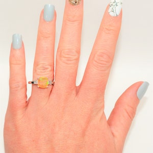 May include: A hand with light blue nail polish on four fingers and a ring with a yellow opal gemstone on the ring finger. The thumb has a light blue nail with a white marble design.