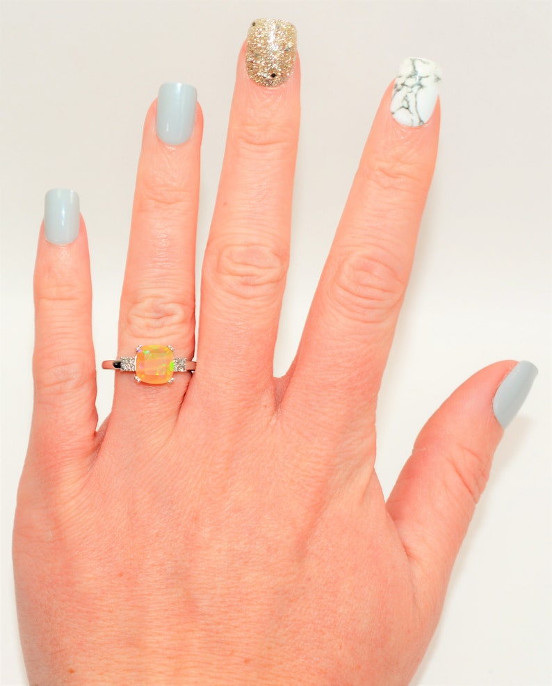 May include: A hand with light blue nail polish on four fingers and a ring with a yellow opal gemstone on the ring finger. The thumb has a light blue nail with a white marble design.