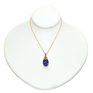 May include: A gold-colored necklace with a pendant featuring a large, oval, deep blue gemstone. The pendant is accented with smaller, clear stones. The necklace is displayed on a white bust.