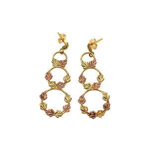Puede incluir: Un par de pendientes de oro con tres círculos entrelazados decorados con hojas en tonos verdes, dorados y rosados.