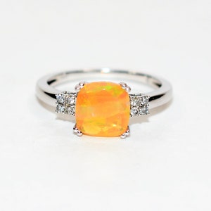 May include: A silver ring with a large, orange opal gemstone and smaller, clear gemstones on either side.