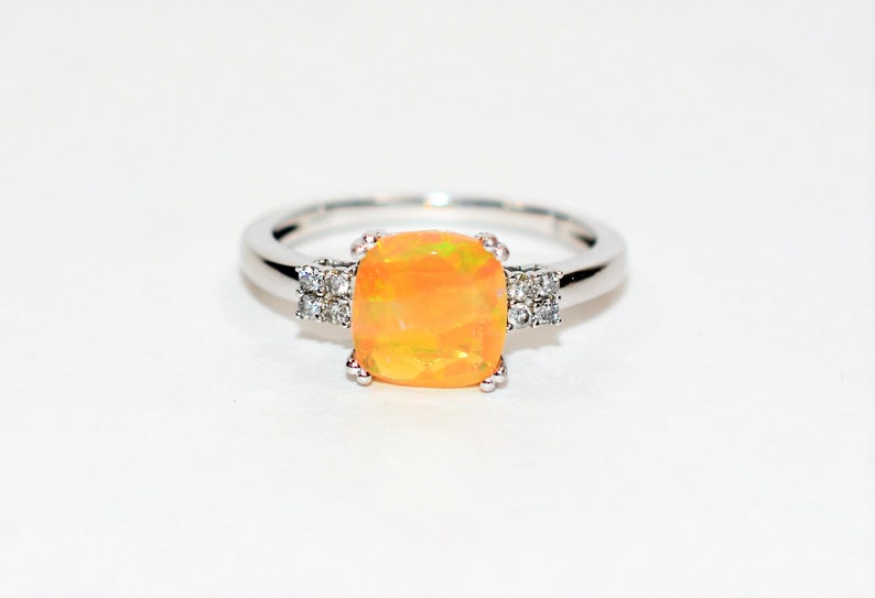 May include: A silver ring with a large, orange opal gemstone and smaller, clear gemstones on either side.