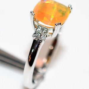 May include: A silver ring with a large, orange opal gemstone and smaller clear gemstones on the band.