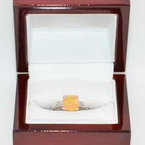 May include: A ring with a large, orange opal gemstone surrounded by smaller, white diamonds. The ring is in a red velvet ring box.