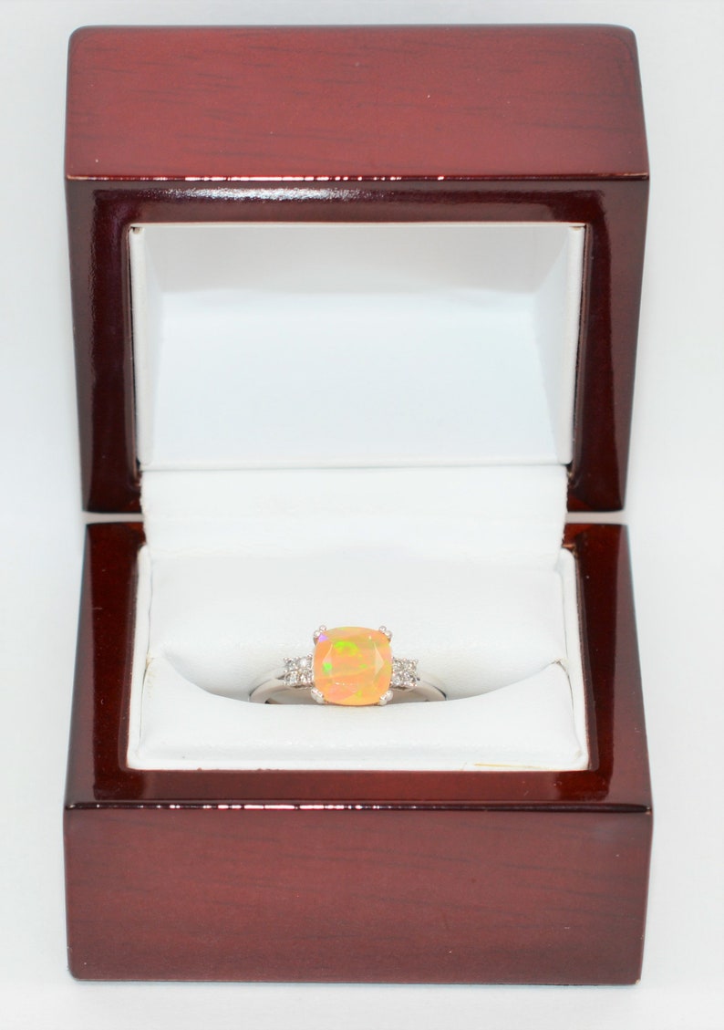 May include: A ring with a large, orange opal gemstone surrounded by smaller, white diamonds. The ring is in a red velvet ring box.