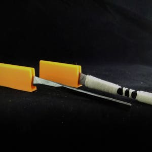 May include: Two orange plastic blocks with a metal rod and white string running through them.