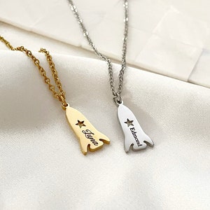 May include: Two silver necklaces with rocket ship pendants. The pendant on the left says "Luna" and the pendant on the right says "Edmond".