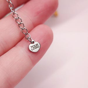 May include: A silver chain necklace with a heart-shaped pendant that says "YOUR LOGO" on it.