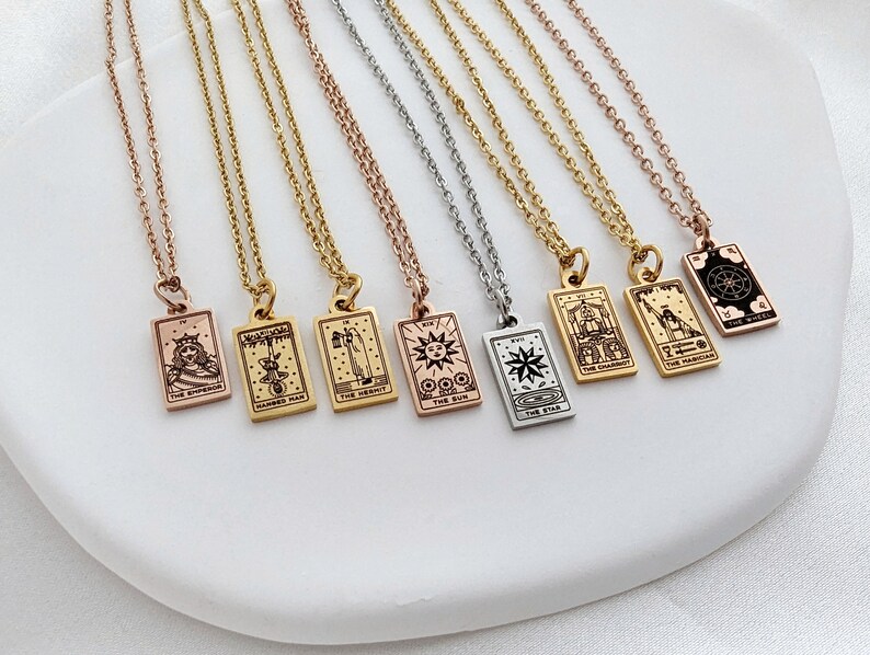 May include: Eight gold, silver, and rose gold necklaces with tarot card pendants. The pendants feature various tarot card imagery, including The Emperor, Hanged Man, The Hermit, The Magician, The Star, The Chariot, The Wheel, and The Sun.