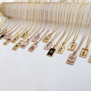 May include: A collection of gold, silver, and rose gold necklaces with small rectangular pendants featuring tarot card symbols. The pendants are engraved with various tarot card symbols, including the sun, the moon, and the world.