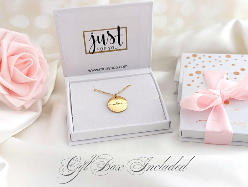 May include: Gold necklace with a round pendant engraved with the name "Madison". The necklace is in a white gift box with the words "just for you" and a website address.