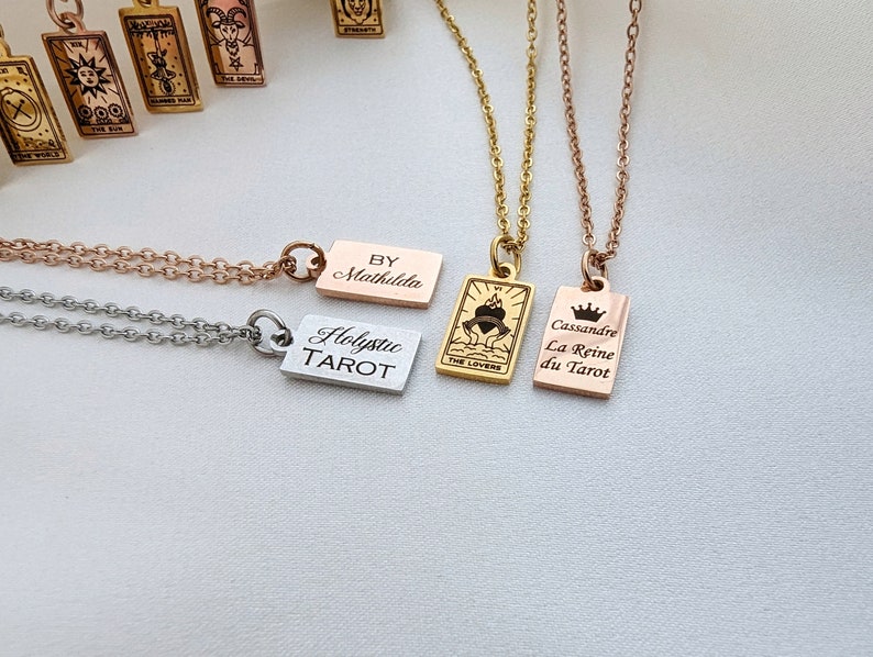 May include: Three gold, silver, and rose gold necklaces with rectangular pendants. The pendants have the words "Holistic Tarot", "By Mathilde", and "Cassandre La Reine du Tarot" engraved on them.