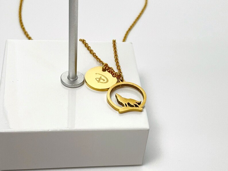 May include: Gold necklace with two pendants. One pendant is a round disc with the Disney logo. The other pendant is a circle with a wolf silhouette inside.