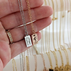 May include: Two silver and gold necklaces with a tarot card pendant. The silver necklace has a rectangular pendant with the text "Holygrail Tarot". The gold necklace has a rectangular pendant with a tarot card image of "The Fool".
