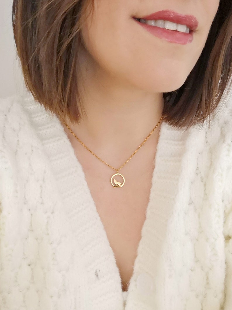 May include: A gold necklace with a pendant featuring a wolf silhouette inside a circle.