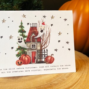 May include: A white card with a watercolor illustration of a house with a red door, a Christmas tree, and two ghosts. The house has a red roof and a black fence. There are pumpkins in front of the house. The card has the text "Twas the night before Christmas, when all through the house All the creatures were stirring, especially the mouse."