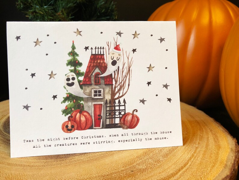 May include: A white card with a watercolor illustration of a house with a red door, a Christmas tree, and two ghosts. The house has a red roof and a black fence. There are pumpkins in front of the house. The card has the text "Twas the night before Christmas, when all through the house All the creatures were stirring, especially the mouse."