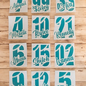 May include: Twelve individual teal vinyl decals featuring baseball-themed numbers with white stitching patterns. Each decal displays a unique number paired with a custom name in white cursive script, including Abigail, Riley, Sofia, Michelle, Rylee, Kennedy, Athena, Shiloh, Ivanna, Emmalee, Camila, and Penelope.