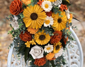 May include: A cascading bouquet of faux flowers in shades of orange, yellow, and white. The bouquet features sunflowers, roses, and other floral arrangements.