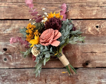 May include: A bouquet of faux flowers in shades of pink, yellow, and green. The bouquet is tied with twine and features a variety of textures, including wood, fabric, and dried flowers.