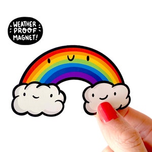 Puede incluir: Un imán con forma de arcoíris con una cara sonriente y nubes en cada extremo. El imán dice "Weather Proof Magnet!"