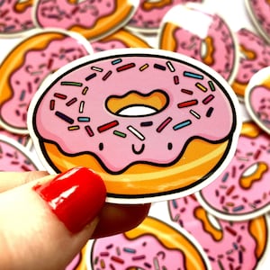 May include: A pink and yellow donut sticker with colorful sprinkles. The donut has a happy face and a cute design.