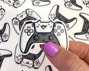 Könnte beinhalten: Ein weißer und schwarzer Videospiel-Controller-Aufkleber mit einem niedlichen Comic-Katzenkopf auf der Vorderseite. Der Controller hat Knöpfe und einen Joystick. Der Aufkleber befindet sich auf einem weißen Hintergrund.