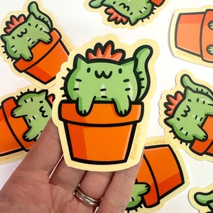 May include: A set of five stickers featuring a green cat with a red flower on its head sitting in a terracotta pot. The cat is depicted as a cactus plant. The stickers are on a white background.