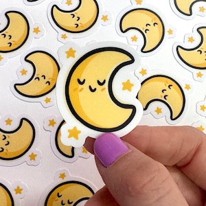 May include: A sheet of stickers featuring yellow crescent moons with closed eyes and a small smile. The moons are surrounded by small white stars.