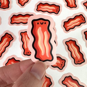May include: A set of pink and red cartoon bacon stickers with a smiling face. The stickers are on a white background.