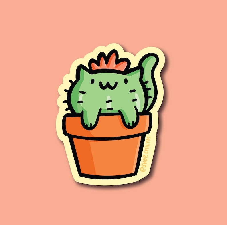 May include: A green cat cactus with a red flower on top, sitting in a terracotta pot. The cactus is wearing a cute smile and has a small tail. The pot has a white outline and the text "@shop.emilym" on the side.