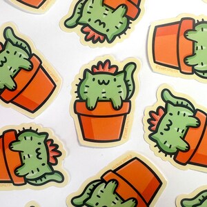 May include: A set of nine stickers featuring a cartoon cat dressed as a cactus in a terracotta pot. The stickers are on a white background. The cat is green and has a pink flower on its head. The pot is orange. The stickers are all different sizes and shapes.