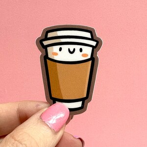 May include: A brown and white coffee cup sticker with a smiling face. The sticker is on a pink background.