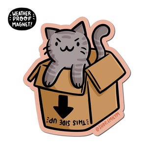 Puede incluir: Un gato gris y blanco a rayas está sentado dentro de una caja de cartón. La caja es marrón y tiene las palabras "This Side Up" escritas en ella. El gato está mirando al espectador con una expresión traviesa. La caja está etiquetada con "Weather Proof Magnet!" y "@shop.emilym".