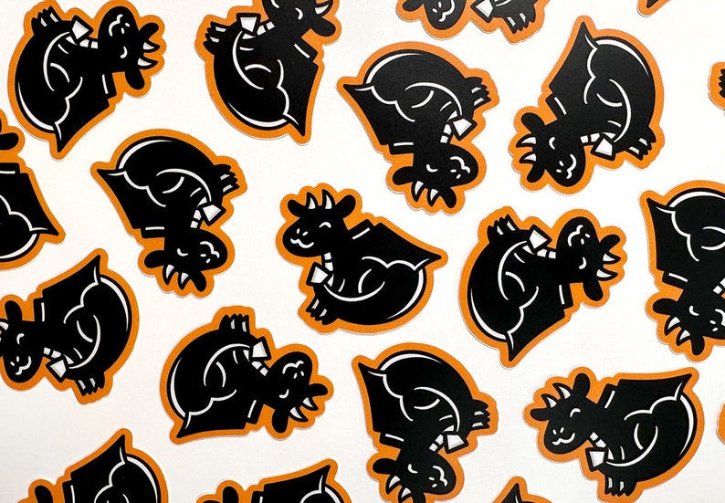 May include: A collection of black and orange stickers featuring a cartoon dragon wearing a bow tie. The dragon is in a variety of poses, including sitting, standing, and flying.