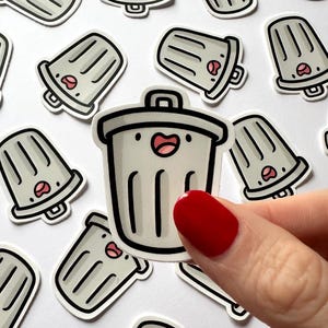 May include: A collection of stickers featuring a cartoon trash can design with a smiling face and a red mouth. The stickers are light gray with black outlines and are scattered across a white background.