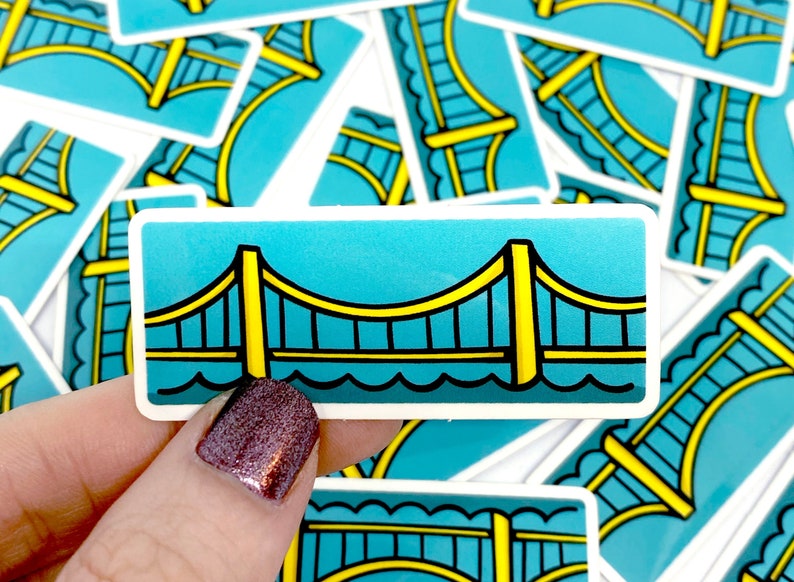 May include: A sticker featuring a yellow bridge with black outlines, set against a blue background. The bridge has a wavy water line at the bottom.