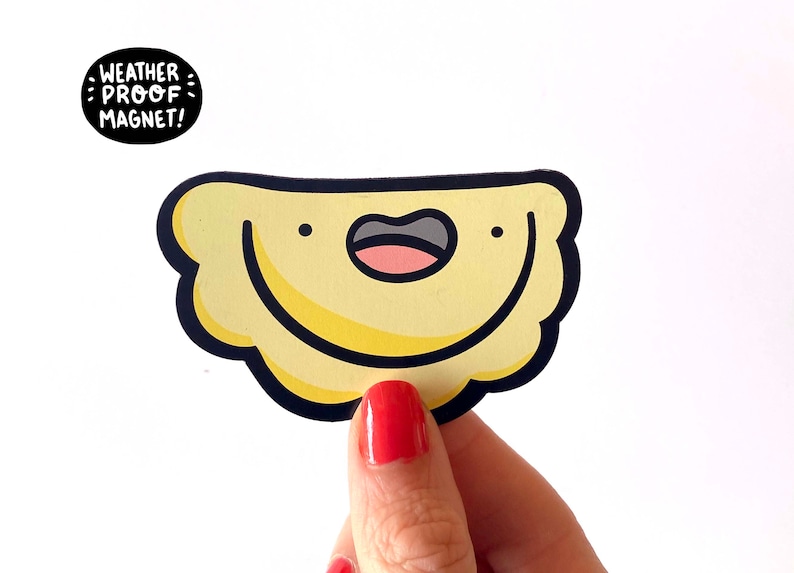 K&ouml;nnte beinhalten: Ein gelber Cartoon-Pierogi mit einem l&auml;chelnden Gesicht, schwarzem Umriss und dem Text "WEATHER PROOF MAGNET!" in einem schwarzen Kreis.