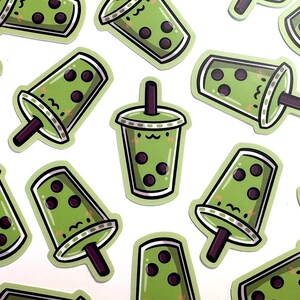 May include: A sheet of green and black bubble tea stickers with a cartoon face and a straw.
