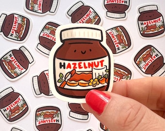 May include: A collection of hazelnut jar stickers. The stickers feature a brown jar with a white lid and the word "HAZELNUT" in red. The jar illustration includes a smiling face and a depiction of hazelnut spread with flowers.
